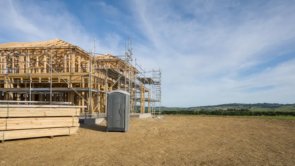 A partly framed two-storey timber house with scaffolding up one side on a cleared site